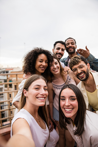 Multicultural cheerful group of carefree friends taking a selfie at a rooftop party.Multiracial beautiful young happy people smiling while taking a picture at a terrace.
