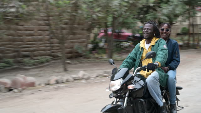 African couple riding electric motorcycle on dirt road in Nairobi
