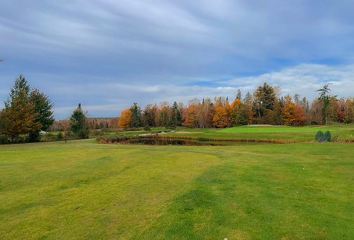 A man strikes a golf ball at a beautiful golf course in fall. Muskoka, Ontario, Canada. Muskoka region is a golf hot sport. Caucasian male golfer in 30s. Unrecognizable man. Demonstrating good balance and proper swing with finish position. 