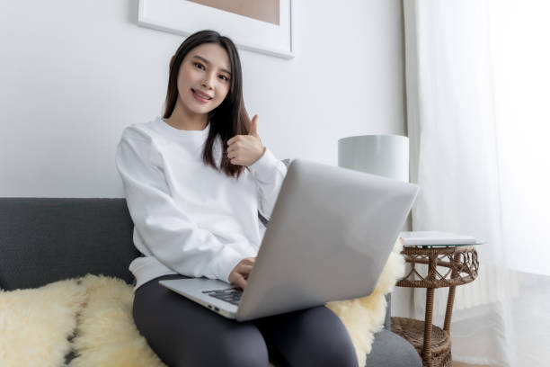 istock young pretty Asian girl sitting on a cozy sofa in the living room while using the computer. 1733953229