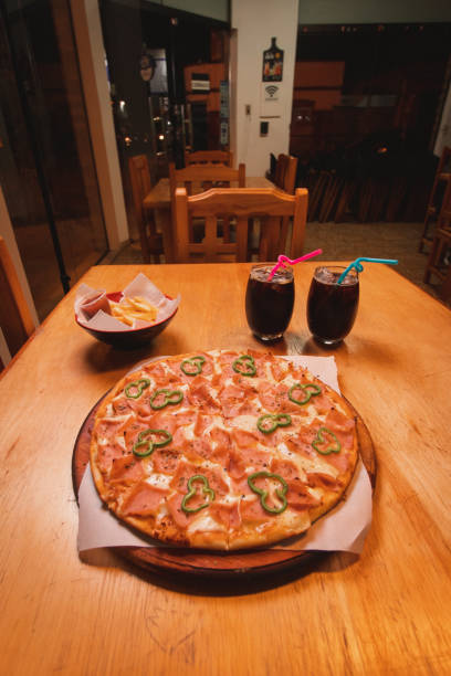 istock Ham and vegetable pizza next to two glasses of soft drinks in a restaurant. 1733954293