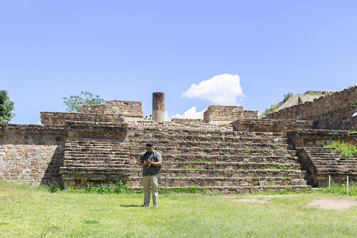 Mexican traveler man using smartphone in front of Monte Alban pyramid