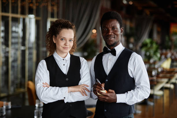 istock Two servers wearing classic tuxedo uniform smiling at camera in restaurant 1734020012