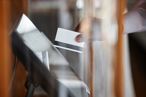 Side view closeup of waiter using computer in restaurant and swiping card putting order in electronic POS system, copy space