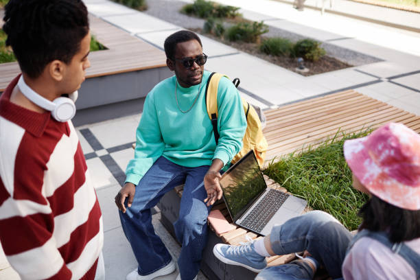 Young Black man as student talking to group of friends on campus