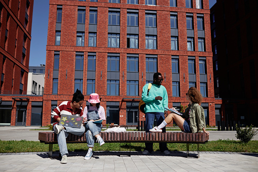 Full length view at group of college students relaxing outdoors in urban setting at college campus, copy space