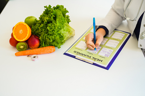 Close-up of woman healthy nutritionist with vegetables and fruits in front of her making meal plan