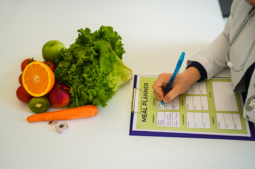 Close-up of woman healthy nutritionist with vegetables and fruits in front of her making meal plan