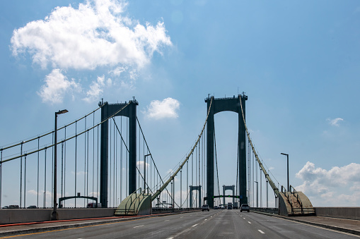 Drivers perspective on Delaware Memorial Bridge near Wilmington, DE, USA in northerly direction with cars on road crossing the Delaware River against a blue sky
