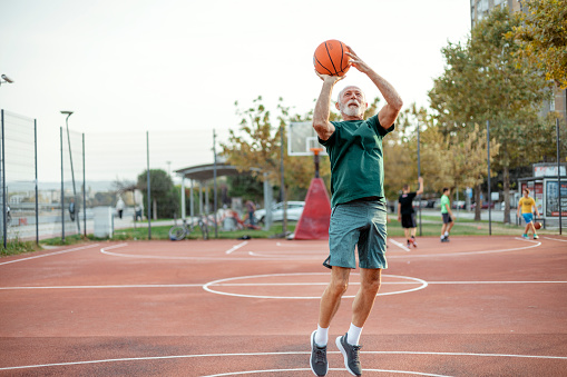 Handsome Determined Caucasian Gray Hair Bearded Senior Man Playing Basketball in the Outdoor Summer Court