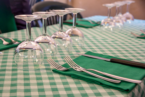 Table setting in a restaurant, close up of forks, knife on a napkin, and empty wine glasses. Served table