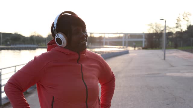 portrait of african american senior woman with headphones listening to music and sportswear in the park