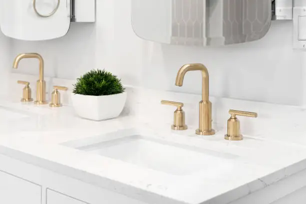 Photo of A bathroom detail with gold faucets and white marble countertop.