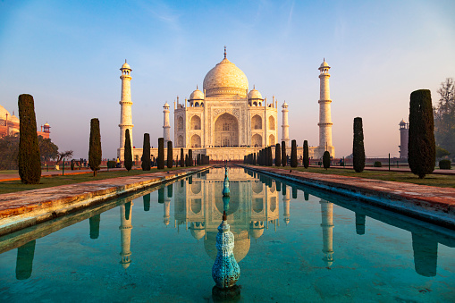 Captured in the early morning light, this image showcases the Taj Mahal as it's rarely seen, bathed in the warm glow of the rising sun. With minimal haze, the iconic white marble monument stands in sharp contrast to the sky, fully revealing its intricate design and grandeur. The photograph captures a tranquil moment at one of the world's most celebrated landmarks, offering a unique perspective of the Taj Mahal's timeless beauty.