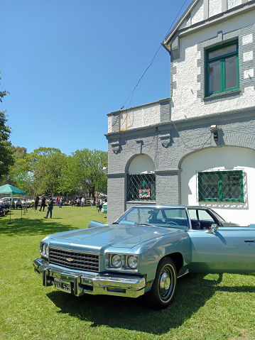 Remedios de Escalada, Argentina - Oct 8, 2023: old blue 1976 Chevrolet Impala sedan by GM, open doors, on the lawn in a garden. Classic car show. Copy space