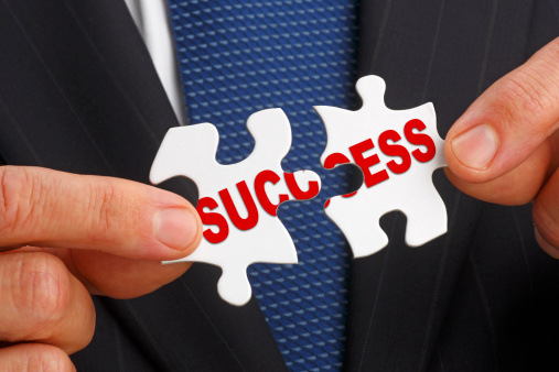 A businessman holding two puzzle pieces together that spell out the word success.