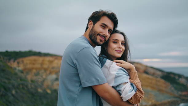 istock Smiling pair looking camera standing hill top in front gray calm ocean close up. 1734202837