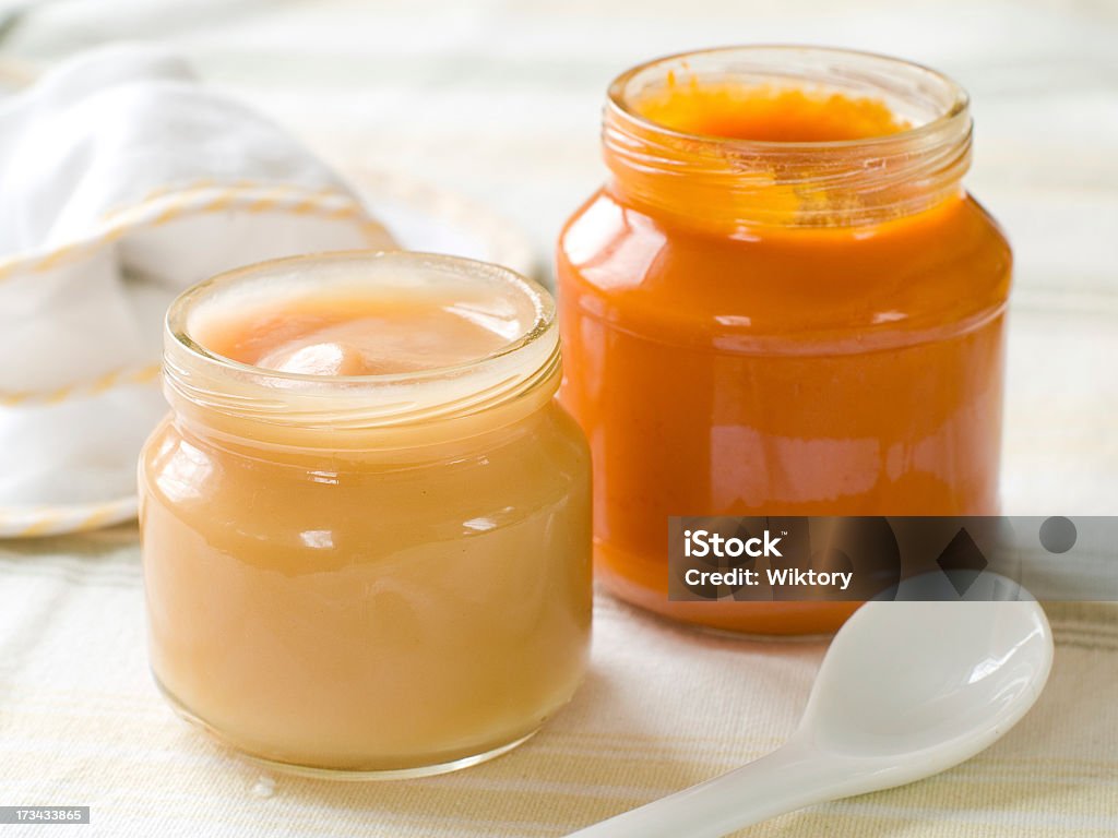 Two open jars of baby food with a spoon in the foreground Fresh, organic pureed fruits for baby. Shot for a story on homemade, organic, healthy baby foods. Baby - Human Age Stock Photo