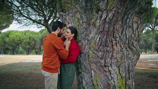 Romantic young couple standing in forest spending weekend together. Loving two people leaning on wide tree enjoying happy date. Tender beautiful pair tourists relaxing on nature feeling closeness love