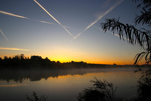 Sunrise at the forest lake with steaming water in the horizon
