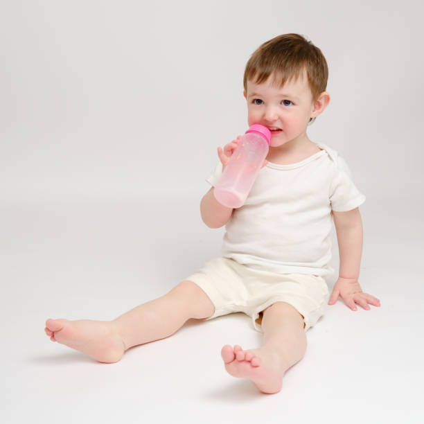 istock Happy baby drinks milk from bottle on studio white background. Resting child eats formula. Kid about two years old (one year nine months) 1734385013