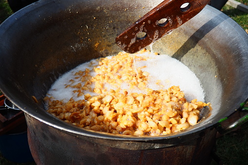 Stirring fat in a large vat on firewood. Pork rinds rendered, fried in fat, baked, roasted to produce pork cracklings or scratchings. Toasted brown cracklings. Large cast iron vat or cauldron