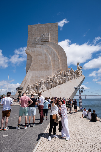 Lisbon, Portugal - April 29, 2023: Tourists taking photos and sightseeing on the north bank of the Tagus River in front of the Monument of the Discoveries.