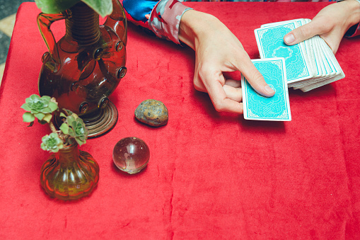 top view of female hands of unrecognizable woman, sitting, placing tarot deck on table, starting therapeutic tarot consultation.