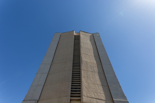 Bottom view perspective of a tall building or business center with a concrete wall against a blue sky.