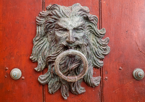 Artful door knocker with face and ring on a reddish-brown wooden door in Cartagena, Colombia, Unesco World Heritage