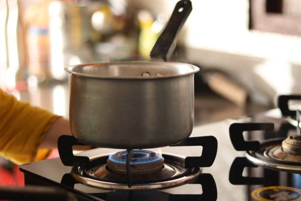 A deep Indian pan pot on the lpg stove with blue flames on in the kitchen