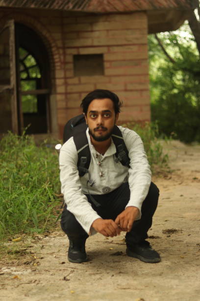 istock An Indian boy with black beard wearing khadi kurta and having a backpack with green vegetation in background sitting on ground 1734740511