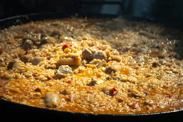 A large paella cooking over fire with a smokey background