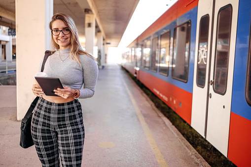 Young business woman on train station holding tablet and having a coffee while waiting for transport
