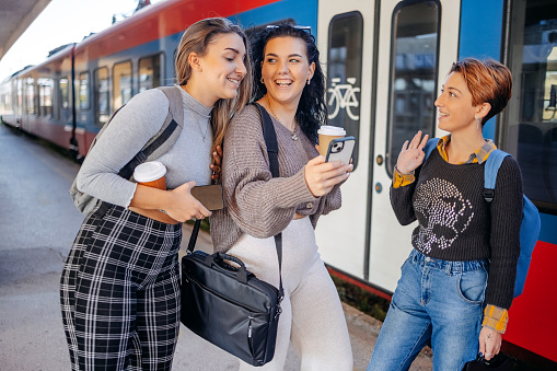 Group of young women friends having fun on railway station while waiting for train to go to work