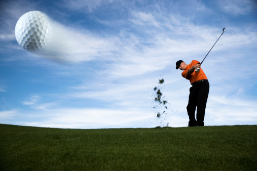 a male golfer hitting a golf ball.  the ball is caught mid flight in motion.  great sky background for plenty of copyspace.