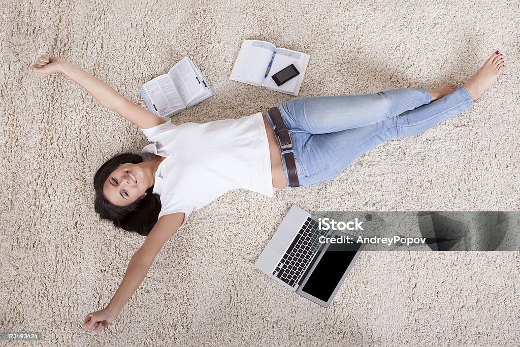 Young woman lying daydreaming Overhead view of a young woman lying on her back on a carpet alongside her laptop daydreaming 20-29 Years Stock Photo