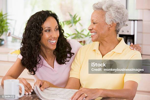 Two Women In Kitchen With Newspaper And Coffee Stock Photo - Download Image Now - 30-39 Years, 40-49 Years, 60-69 Years