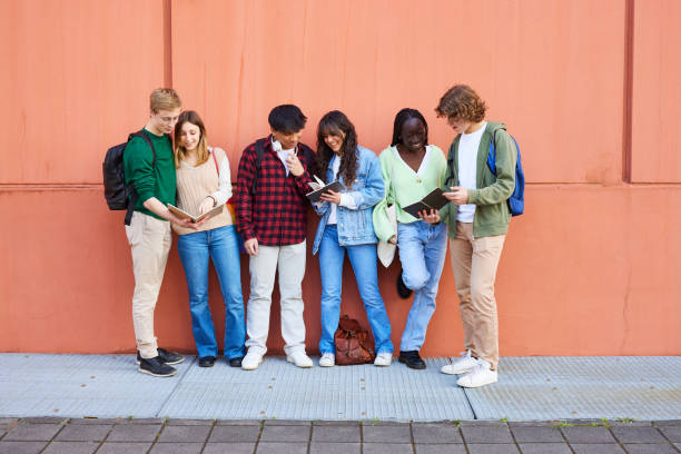 Students discussing over books against red wall in campus