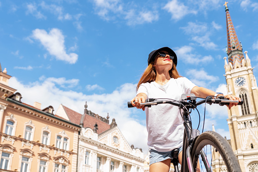 Urban young woman enjoying a bike ride around the city in summer.