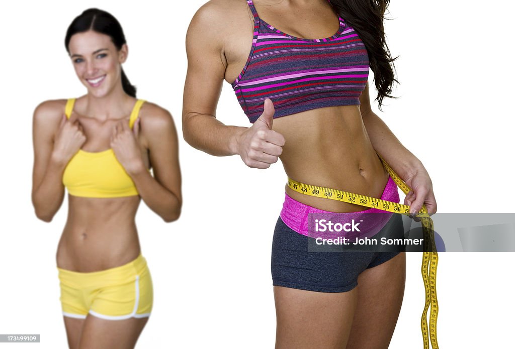Weight loss and fitness concept Closeup of a woman measuring her waist with another woman in the background smiling and both wearing fitness clothing  20-24 Years Stock Photo