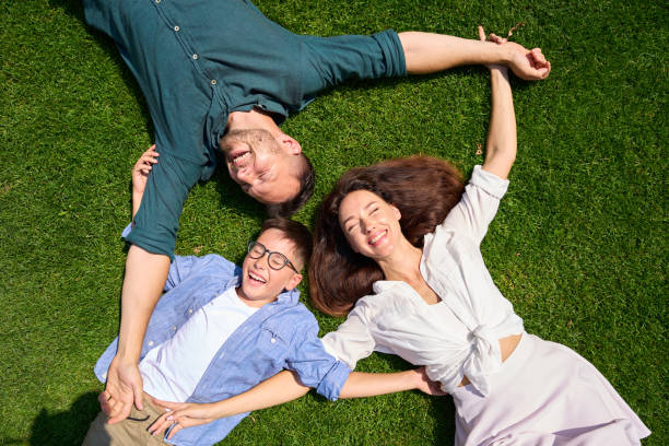 une jolie famille s’étreint sur la pelouse - glasses grass women lying on front photos et images de collection