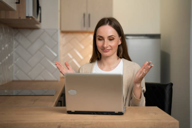 istock A positive student, smiling, sitting at a table with a laptop in the kitchen, studying at home and waving at the screen, watch an online webinar 1735017362