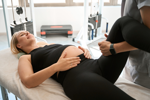 Cute expectant mother at a comfortable chiropractic session, specialist working on her feet