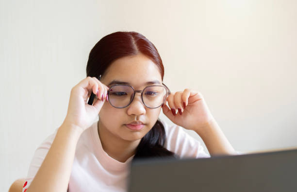 istock Young Asian girl college student adjusting her glasses and using laptop computer from home 1735041054