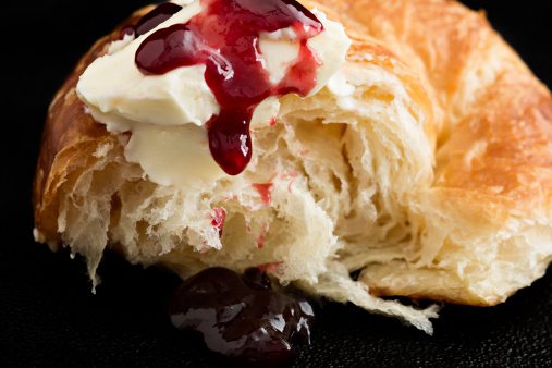 A close up shot of a piece of croissant with some butter and raspberry jam.
