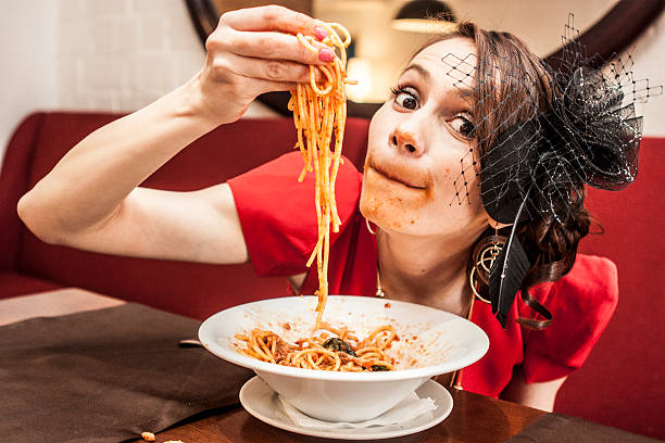 Beautiful girl in a red dress and black hat eats pasta.