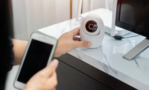 istock Female hands holding smart phone and installing wireless CCTV camera at house for security. 1735049050