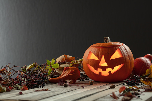 Halloween pumpkin head jack lantern with dried-up leaves. Halloween holidays art design, celebration. Carved Halloween pumpkin with burning candle.