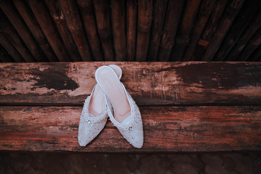 Close-up of a pair of white wedding shoes on a rustic wooden bench